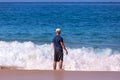 A Caucasian man in a blue t-shirt, beige baseball cap and long black board short standing in a crushing waves Royalty Free Stock Photo