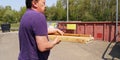 Caucasian man carries wooden planks to throw into huge containers at station of collection of large-size garbage