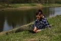 Caucasian man with dreadlocks and beard lying in clearing on river bank in spring park and working on laptop. Serious and