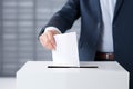 caucasian man in formal suit put paper vote into white mock up ballot box. Voting concept