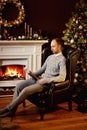 Caucasian man in grey clothes sits in chair by burning fireplace and reads magazine Royalty Free Stock Photo