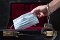 Caucasian man hand with handcuffs stuffing face mask into a safety briefcase