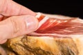 Caucasian man hand takes slices from Serrano ham