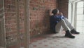 Man sits against brick wall in shabby entrance near window and it freezing
