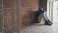 Man sits against brick wall in shabby entrance near window and sleeps