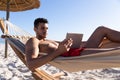Caucasian man lying on a hammock and using a digital tablet at the beach. Royalty Free Stock Photo