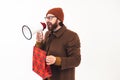 Caucasian man with a megaphone. Studio shot of a millennial bearded guy in a beanie and brown coat holding a loudspeaker