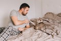 Caucasian man playing with cat. Angry furious cat biting scratching owner master hand. Guy lying on bed at home with oriental cat