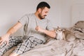 Caucasian man playing with cat. Angry furious cat biting scratching owner master hand. Guy lying on bed at home with oriental cat
