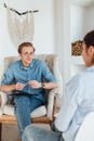 Caucasian man psychologist in eyeglasses sitting in a chair at the workplace, listens to the patient and takes notes