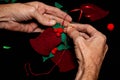 A caucasian man`s hands sewing a holly sprig and ribbon hanger to a felt Christmas Bell ornament. Black background with room for