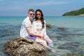 Caucasian man sit on the rock with Asian woman and look at camera with smiling on day time during honey moon vacation or holiday