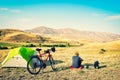 Caucasian man sit by touring bicycle in mountains on side of green tent have break time rest in morning. Solo travel journey. Long Royalty Free Stock Photo