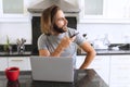 Caucasian man sitting in kitchen using laptop and talking on smartphone Royalty Free Stock Photo