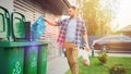 Caucasian Man is Throwing Away Two Plastic Bags of Trash next to His House. One Garbage Bag is Royalty Free Stock Photo