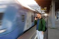 Caucasian man traveler in green windbreaker and with backpack stands on platform talking on the phone, electric commuter train