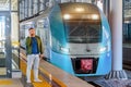 Caucasian man traveler in green windbreaker and with backpack stands on rail road platform talking on the phone, electric commuter