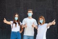 Caucasian man and two women in white T-shirts and anti-virus masks showing their thumbs up outdoors Royalty Free Stock Photo