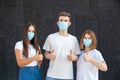 Caucasian man and two women in white T-shirts and protective masks from viruses showing thumbs up outdoors Royalty Free Stock Photo