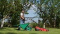 Caucasian man unload grass from lawn cutter machine bag into wheelbarrow. Meadow lawn cutting. Landscape worker
