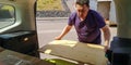 Caucasian man unloads wooden planks from car trunk to station of collection of large-size garbage on spring sunny day