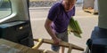 Caucasian man unloads wooden planks from car trunk to station of collection of large-size garbage on spring sunny day