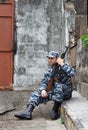 Caucasian man in urban warfare sitting with rifle protecting gat Royalty Free Stock Photo