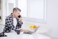 Caucasian man using laptop and phone in kitchen Royalty Free Stock Photo