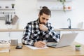 Caucasian man wearing checkered shirt writing on document.