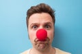 Caucasian man wearing clown red nose isolated on blue background. Royalty Free Stock Photo