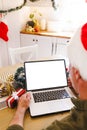 Caucasian man wearing santa hat, sitting at table in kitchen, using laptop with copyspace Royalty Free Stock Photo