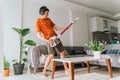 Caucasian man wearing wireless headphones plays rocks air guitar on vacuum cleaner. Male doing home chores with fun Royalty Free Stock Photo