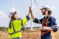 Caucasian man and woman engineers in uniform discuss with shaking hands stand near wind turbines ecological energy industry,