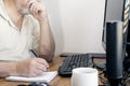 Caucasian man writing with a pen on a notepad while looking at his PC monitor Royalty Free Stock Photo