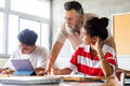 Caucasian mature adult man teacher with beard assisting teen high school students in class using tablet Royalty Free Stock Photo