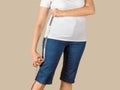 Caucasian mature adult woman dressed in a white T-shirt and a blue denim capris is going to shorten them and drawing a cut line on Royalty Free Stock Photo