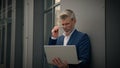 Caucasian mature retired business man with laptop working distant online work in city leaning to wall off company office Royalty Free Stock Photo