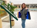 Caucasian mature woman standing in shopping center carrying many paper bags in hands and looking at camera in good mood