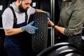 caucasian mechanic holding a tire and showing wheel tires at car repair service and auto store shop Royalty Free Stock Photo