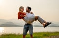 Caucasian man stand and carry his lover woman with love and stay near lake in park with sunset light and they look happiness Royalty Free Stock Photo