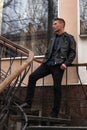 Caucasian  men  stands on the steps outside and looks straight away.  Dressed into black trousers, T-shirt, leather jacket Royalty Free Stock Photo