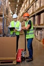 two male warehouse workers with hand pallet jack lift stand discussing, temwork