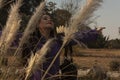 Face of a Mexican Caucasian woman caressed by tails of feathers contryside plants while outstretched arm carries her bag