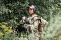 Military lady woman in tactical gear posing for photo in forest during summer.