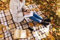 Caucasian millennial female in raincoat makes notes in notebook, sits on plaid with thermos, phone with blank screen Royalty Free Stock Photo