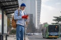 Caucasian millennial guy standing at bus stop checking public transport schedule in mobile app