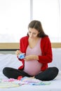 Caucasian millennial young happy female prenatal pregnant mother in casual pregnancy outfit jacket sitting smiling on bed in Royalty Free Stock Photo
