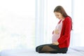 Caucasian millennial young happy female prenatal pregnant mother model in casual pregnancy outfit jacket sitting alone on bed in Royalty Free Stock Photo
