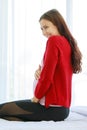 Caucasian millennial young happy female prenatal pregnant mother model in casual pregnancy outfit jacket sitting alone on bed in Royalty Free Stock Photo