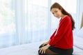 Caucasian millennial young happy female prenatal pregnant mother model in casual pregnancy outfit jacket sitting alone on bed in Royalty Free Stock Photo